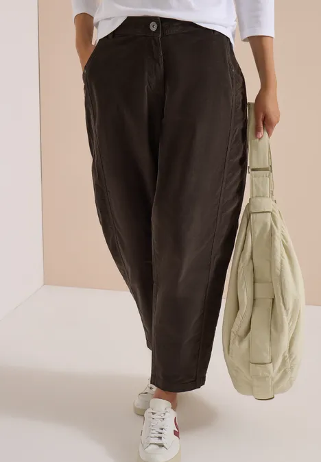 Schwarze, weit geschnittene Hose, weiße Sneaker und eine große, beige Umhängetasche.