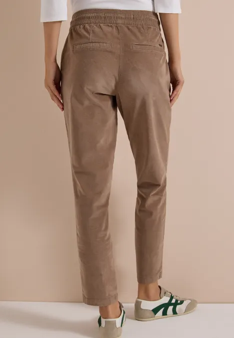 Mid Waist Slim Leg Hose im Casual Fit earthy taupe Rückenansicht einer Person in hellbrauner, elastischer Bundhose und weißen Sneakern mit grünen Streifen.