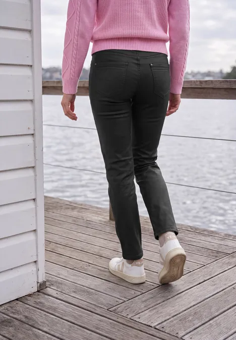 Mid Waist Straight Leg Hose im Slim Fit Black Person in rosa Pullover und schwarzen Hosen läuft auf einem Steg am Wasser.