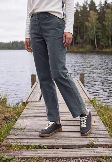 Person in Jeans und Sneakers steht auf einem Steg am See, umgeben von Wald