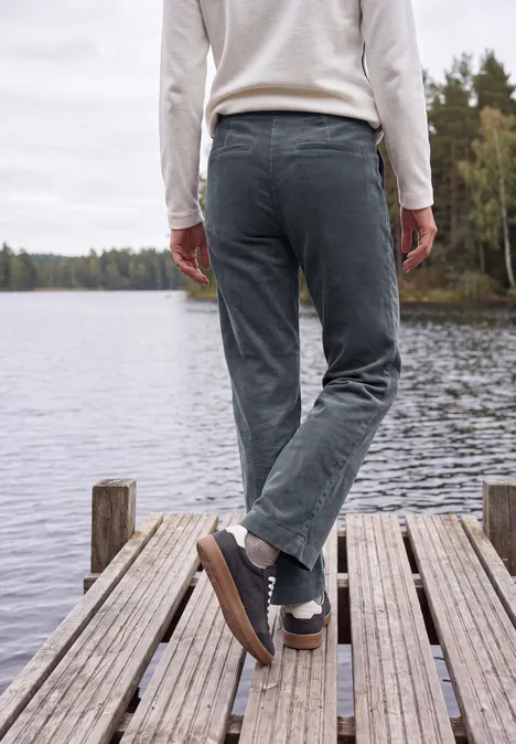Eine Person steht auf einem Holzsteg am See, Blick aufs ruhige Wasser und die umliegenden Bäume.