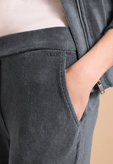 Nahaufnahme einer dunkelgrauen Cordhose mit Hand in der Tasche und passender Jacke.