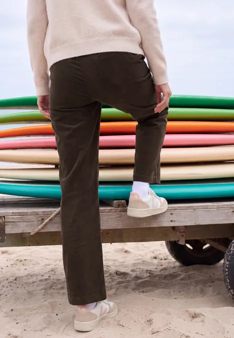 Person steigt in Freizeitkleidung am Strand auf einen Anhänger mit bunten Boards.