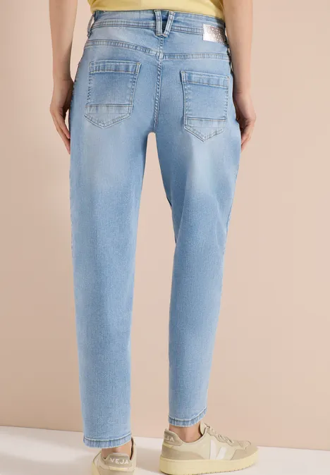 Rückenansicht: Person trägt hellblaue, relaxed-fit Jeans mit schmalem Beinabschluss und beigefarbenen Sneakern.