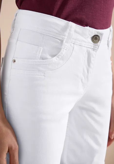 Weiße Damenjeans mit Taschen und Knopf, kombiniert mit burgunderfarbenem Oberteil.