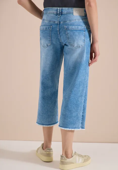 Rückansicht einer Person in hellblauen, weiten Cropped-Jeans mit Fransen und beigen Sneakern