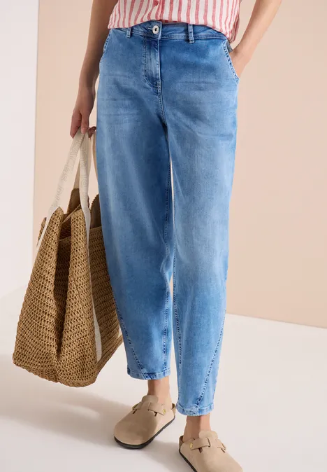Helle Jeans mit weitem Bein, gestreiftes Oberteil, geflochtene Basttasche und bequeme Slipper.