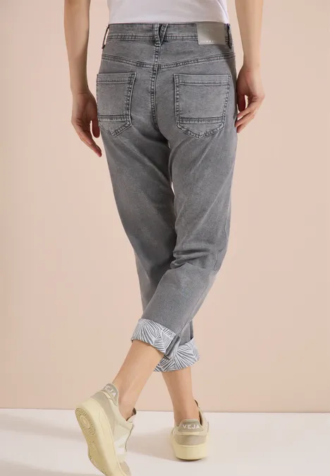 Rückansicht einer Person in grauen, hochgekrempelten Jeans und Sneakern vor neutrem Hintergrund