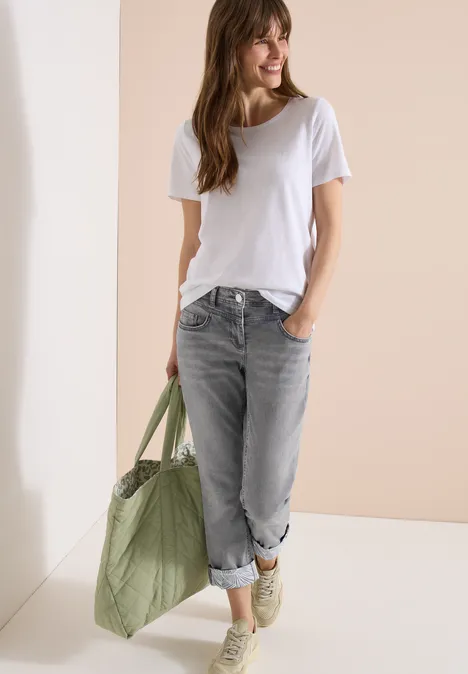 Frau trägt weißes T-Shirt, graue Jeans, olivgrüne Tasche und weiße Sneaker.