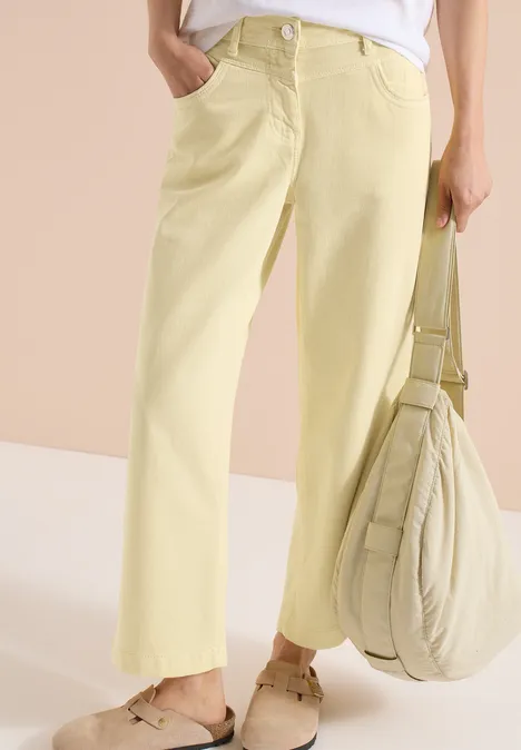 Helle gelbe, weite Damenhose mit aufgesetzter Tasche, dazu passende Stofftasche und bequeme Sandalen.