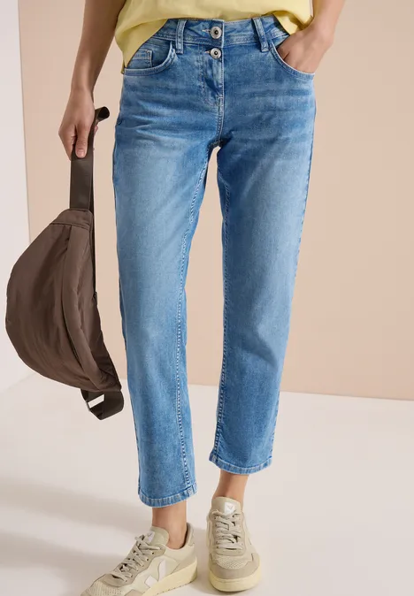 Een persoon draagt blauwe jeans, lichtbeige sneakers en houdt een bruine tas vast.