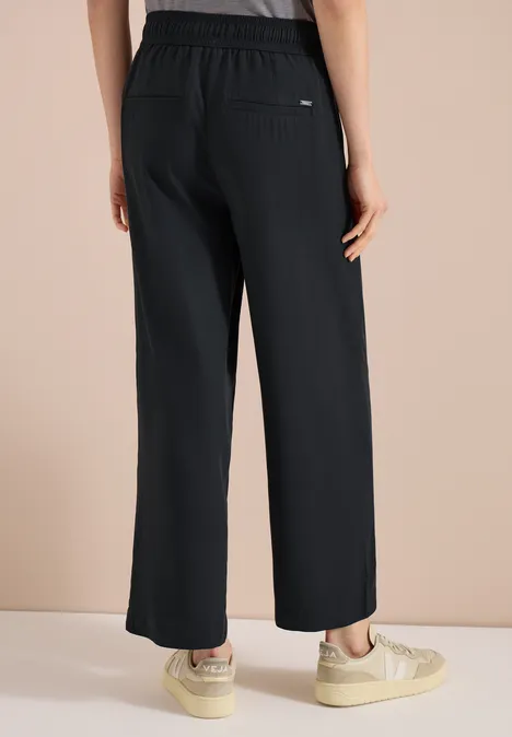 Vue de dos d'une personne portant un pantalon noir ample à taille élastique et poches latérales.