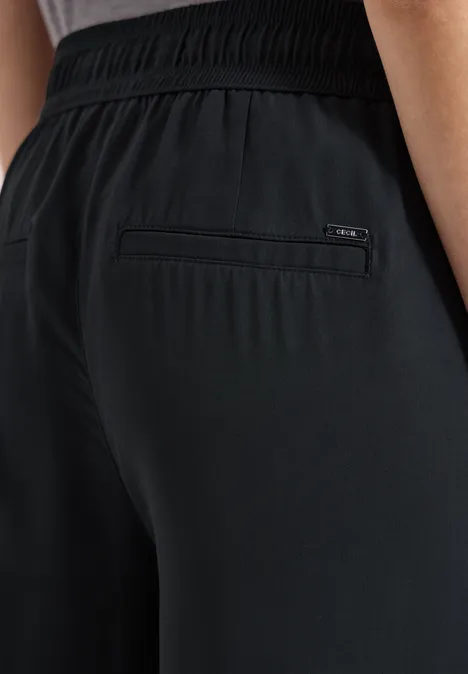 L’image montre une personne portant un pantalon noir extensible avec une poche zippée à l’arrière.