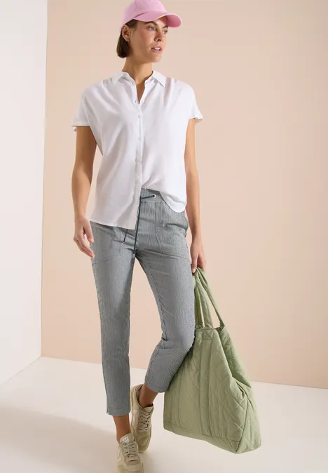 Dame in wit shirt, lichtblauwe jeans en sneakers, draagt een grote groene gewatteerde tas voor een neutrale achtergrond.