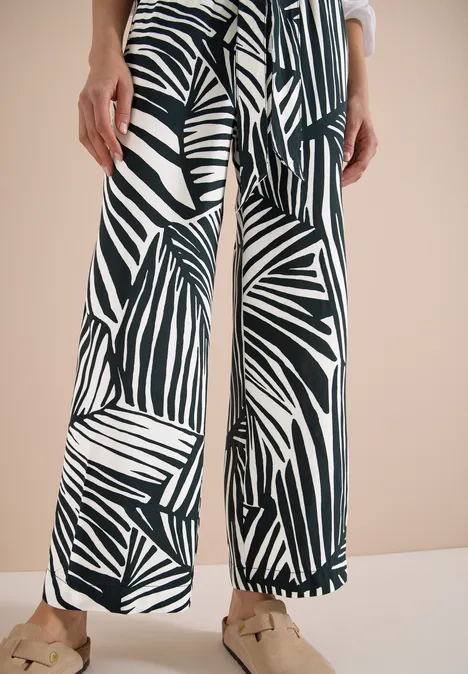 Schwarz-weiße Palmenblatt-Hose mit weitem Bein, kombiniert mit beigen Loafern.