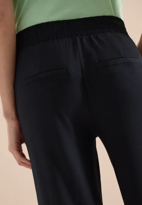 Achteraanzicht van een persoon in donkerblauwe broek met elastische tailleband en opgestikte achterzakken.