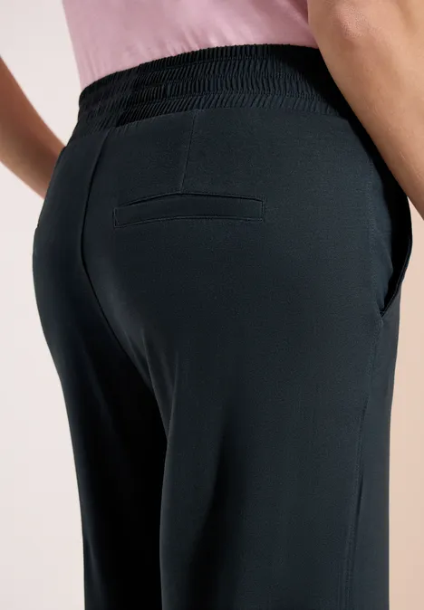 Close-up van een model van achteren in een zwarte broek met achterzak en steekzakken aan de zijkanten.