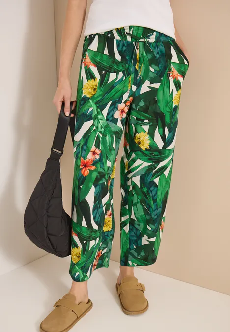 High Waist Wide Leg Hose im Loose Fit khaki Grüne Stoffhose mit tropischem Blattmuster, lässiger Schnitt, schwarze Tasche und beige Slipper.