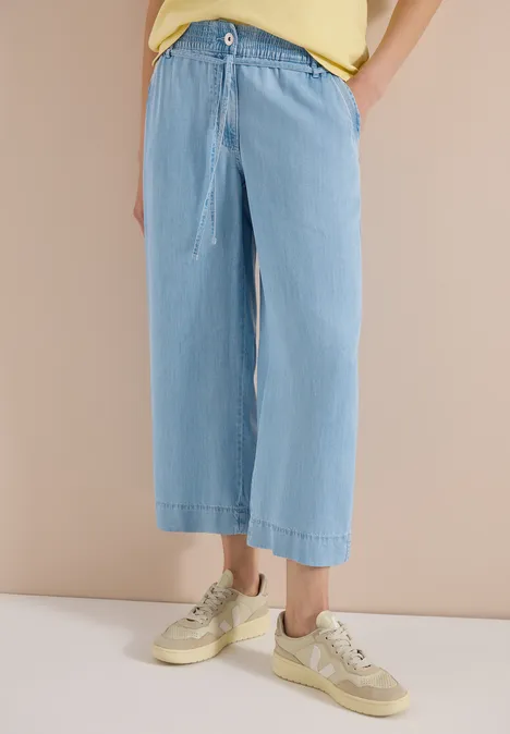 Locker sitzende, hellblaue, weite Jeans mit Kordelzug bis knapp über die Knöchel, kombiniert mit beigen Sneakern.