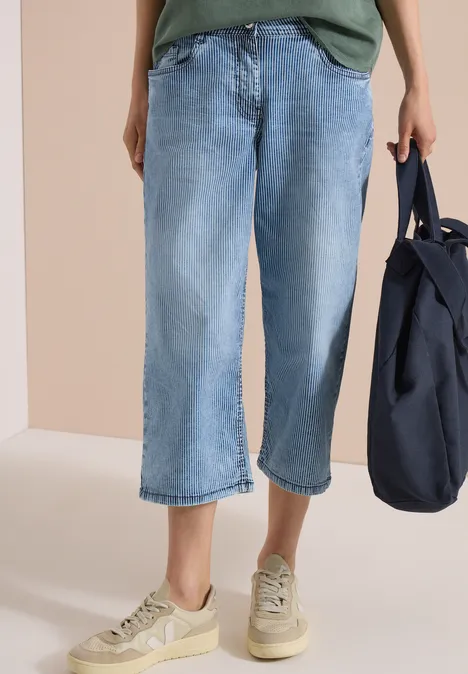 Personne portant un jean court large bleu clair, des baskets beiges et un sac bleu foncé