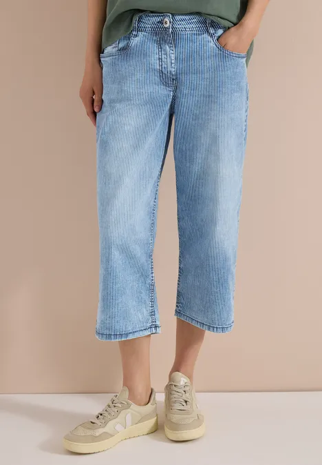 Jean 7/8 ample bleu clair porté avec des baskets beige décontractées.