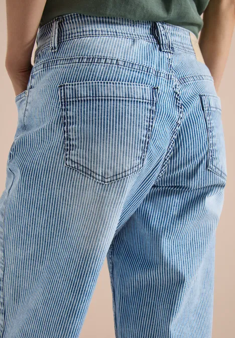 Gros plan d’une personne portant un jean bleu clair à rayures, vue de dos.