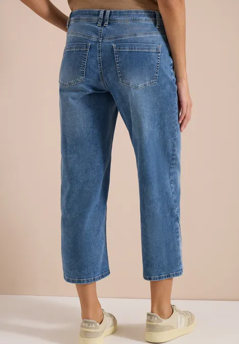 Rückansicht einer Person in blauen, hochgeschnittenen, weiten Cropped-Jeans und weißen Sneakers.