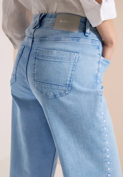 Close-up van de rug en heupen van een persoon in een lichtblauwe spijkerbroek.