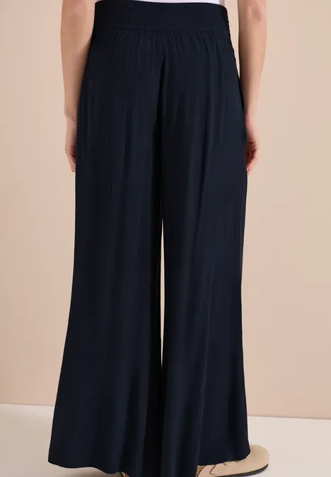 Personne vue de dos portant un pantalon large bleu foncé en tissu fluide à taille haute.