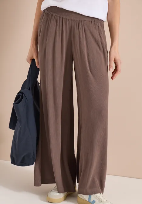 Frau trägt fließende, braune, weite Hose mit hohem Bund und weiße Schuhe, lässig und bequem.