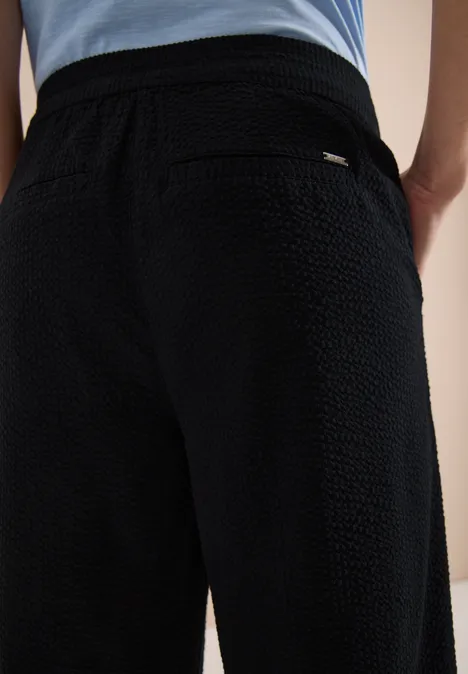 Schwarze, strukturiert wirkende Hose mit elastischem Bund und Po-Tasche aus dicht gewebtem Stoff.