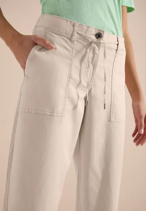 Beige Weite Hose mit Eingrifftaschen, Tunnelzug und Knopf, kombiniert mit hellgrünem Oberteil.