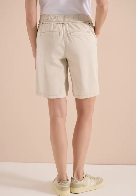 Mid Waist Wide Leg Shorts im Loose Fit pearl beige Rückansicht einer Person in hellen Bermudashorts und Sneakern vor beigem Hintergrund.
