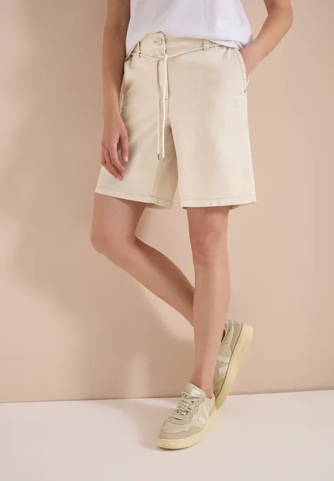 Mid Waist Wide Leg Shorts im Loose Fit pearl beige Person trägt weißes T-Shirt, kniehohe beige Shorts und helle Sneaker.