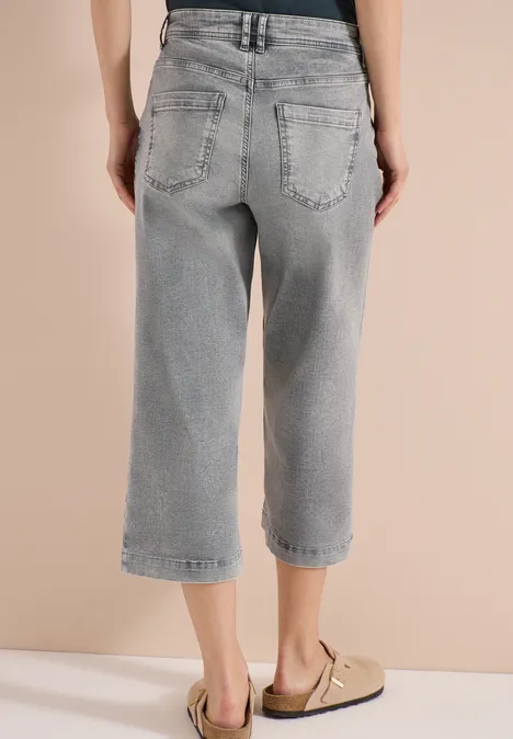 Achteraanzicht van iemand in grijze, losse, kniebroeklange jeans en beige sandalen.