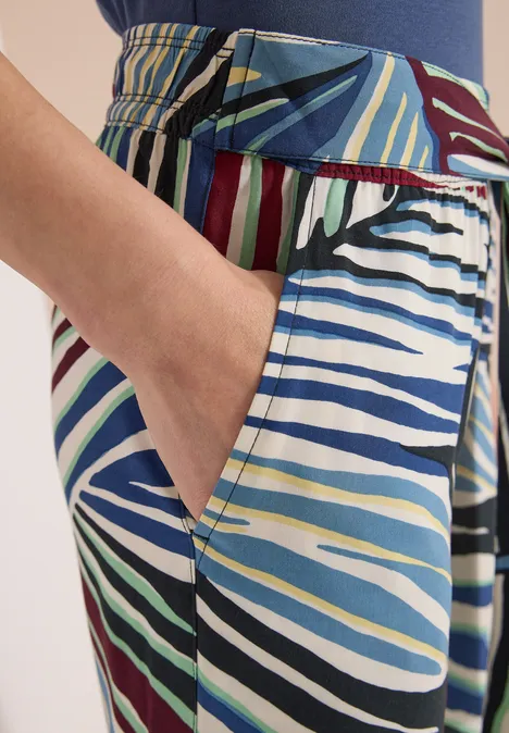 Eine Hand in der Tasche einer bunten, gestreiften Hose mit markanten Farbstreifen.