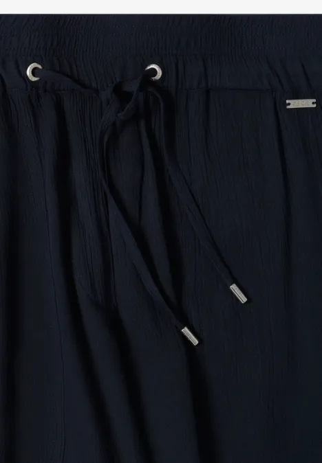 Nahaufnahme einer schwarzen, texturierten Hose mit elastischem Bund und Kordelzug mit silbernen Enden.