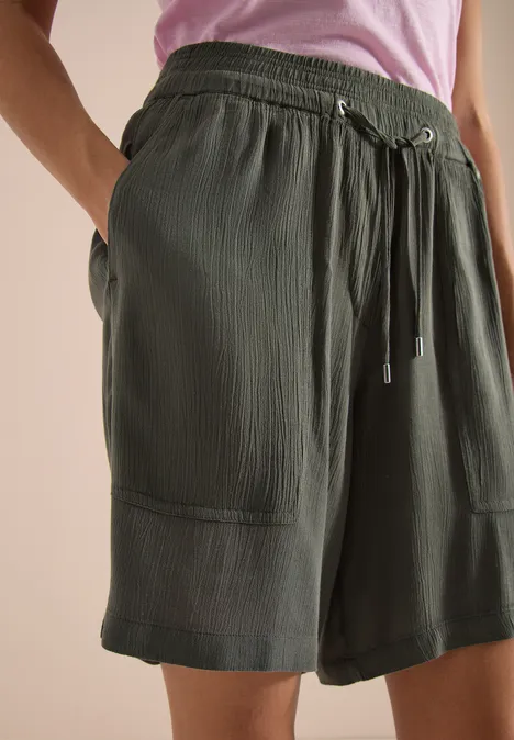 Olivefarbene Shorts mit Kordelzug, aufgesetzten Taschen und leichter Rippstruktur, locker geschnitten, knieumspielend.