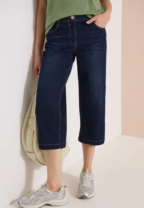 Damen-Jeans-Culotte aus dunklem Denim, weiter Schnitt, knöchellang, mit Sneakers kombiniert.
