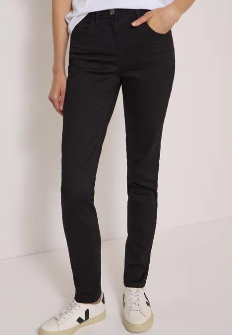 Jean taille haute Slim Leg, coupe slim Black Schlanke schwarze Hose bis zum Knöchel, kombiniert mit weißen Sneakers, vor neutralem Hintergrund.
