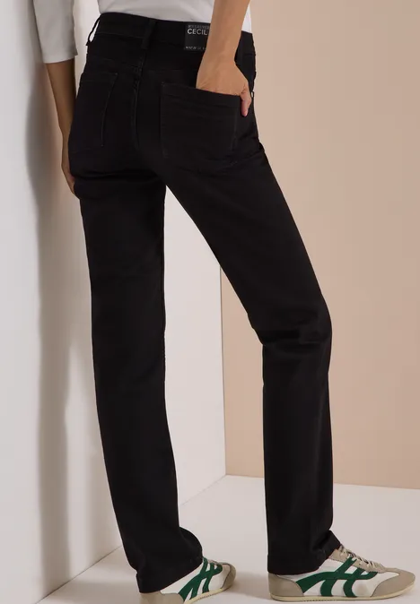 Schwarze, gerade geschnittene Jeans, kombiniert mit weißen Sneakern mit grünen Akzenten.