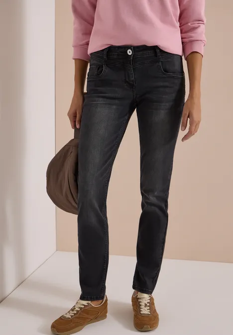 Vrouw met roze trui, donkergrijze jeans, bruine sneakers en een draagtas.