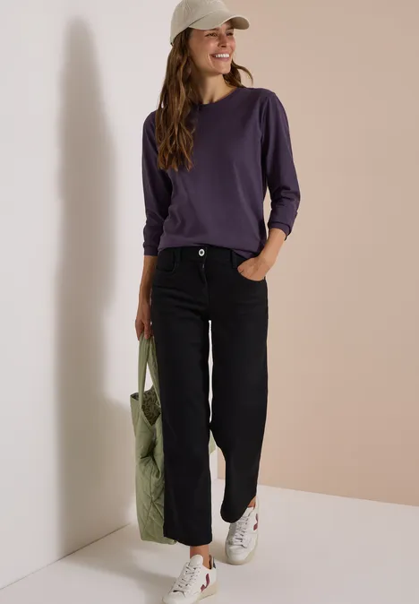 Frau in Casual-Outfit mit Tasche steht vor einer Wand