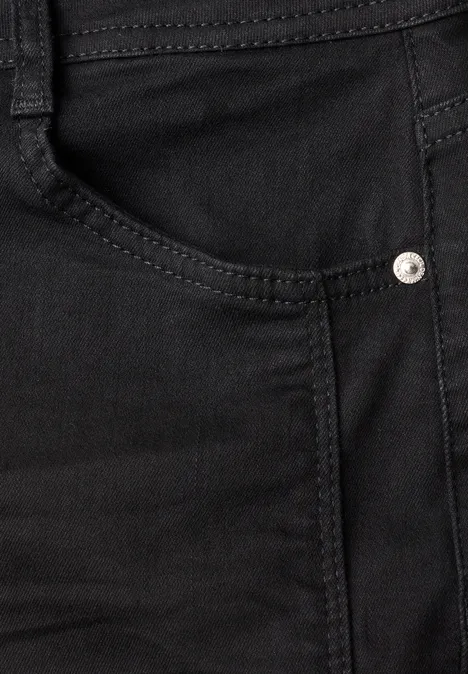 Close-up van een zwarte spijkerbroek met zichtbare zak, steken en metalen klinknagel.