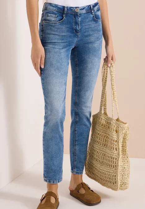 High Waist Slim Leg Jeans im Slim Fit light blue used wash Frau trägt blaue Jeans, braune Schuhe und hält eine geflochtene Basttasche.