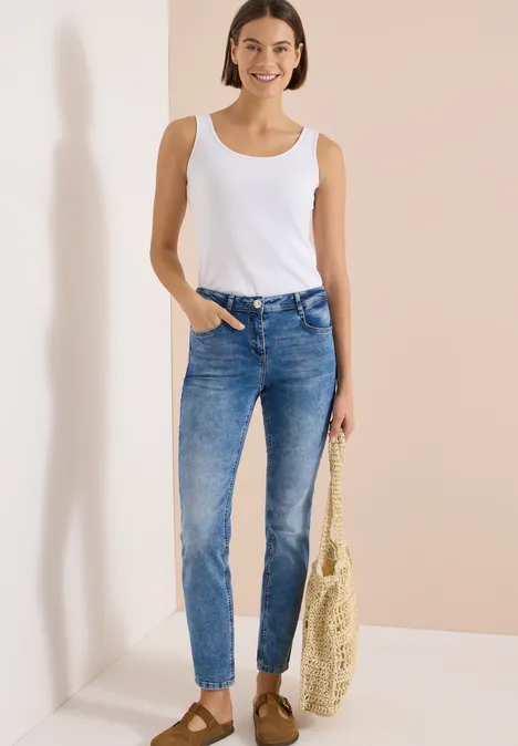 High Waist Slim Leg Jeans im Slim Fit light blue used wash Eine Frau in blauen Jeans und weißem Tanktop mit Basttasche vor hellem Hintergrund.