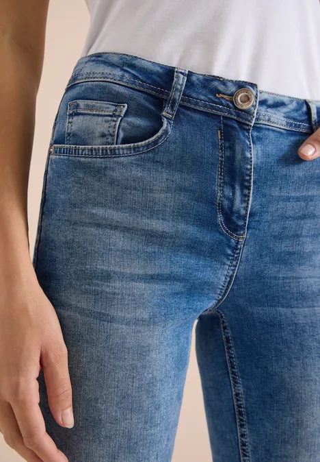 High Waist Slim Leg Jeans im Slim Fit light blue used wash Nahaufnahme einer Person mit blauen Jeans und weißem Shirt, Hand an der Hüfte.
