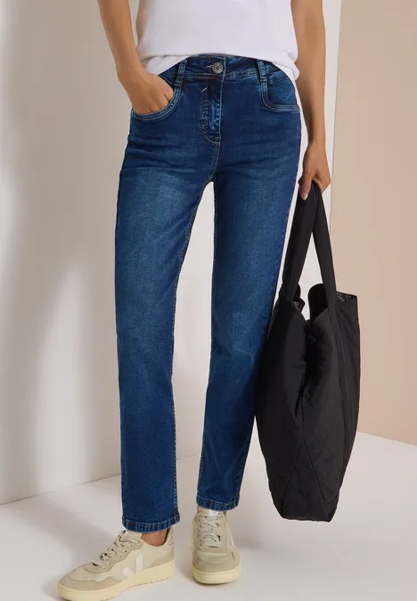 Jeans met High Waist en smalle pijpen in Slim Fit mid blue wash Person trägt blaue Straight-Leg-Jeans, weiße Sneaker und hält eine schwarze Tasche.