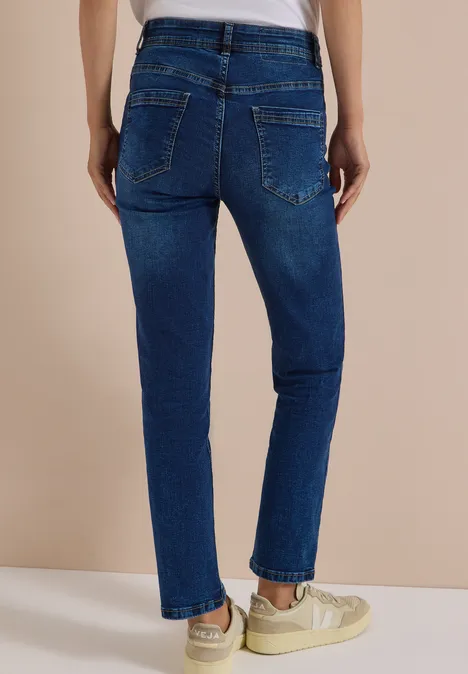 Jeans met High Waist en smalle pijpen in Slim Fit mid blue wash Rückansicht einer Person in dunkelblauen Jeans und weißen Sneakern vor beigem Hintergrund.