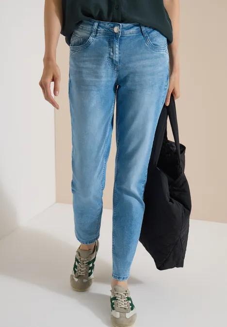 Mid Waist Slim Leg Jeans im Casual Fit light blue wash Unterkörper einer Person in hellblauen Jeans, Sneakern und schwarzer Tasche.